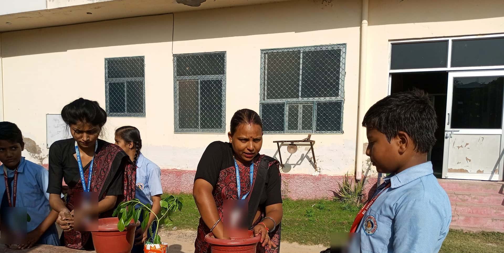 Students and two women plant saplings in red pots on a platform in the schoolyard