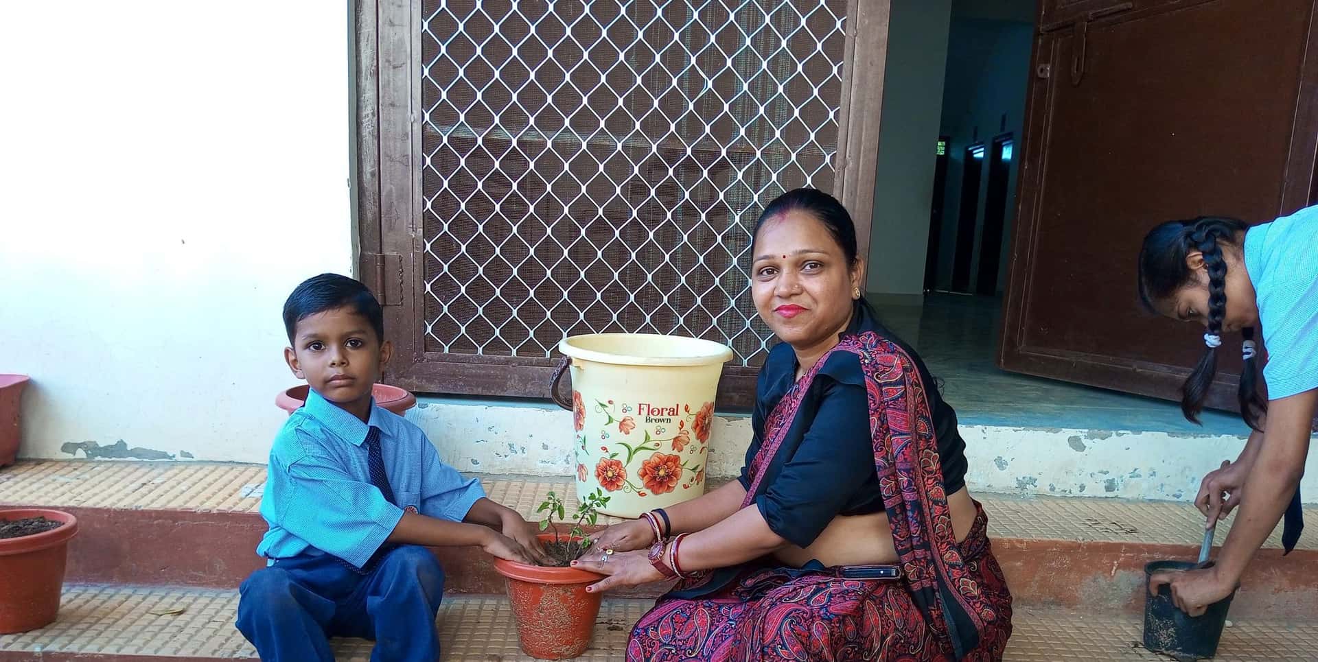 A student and a woman on the school steps with their hands on a newly potted sapling