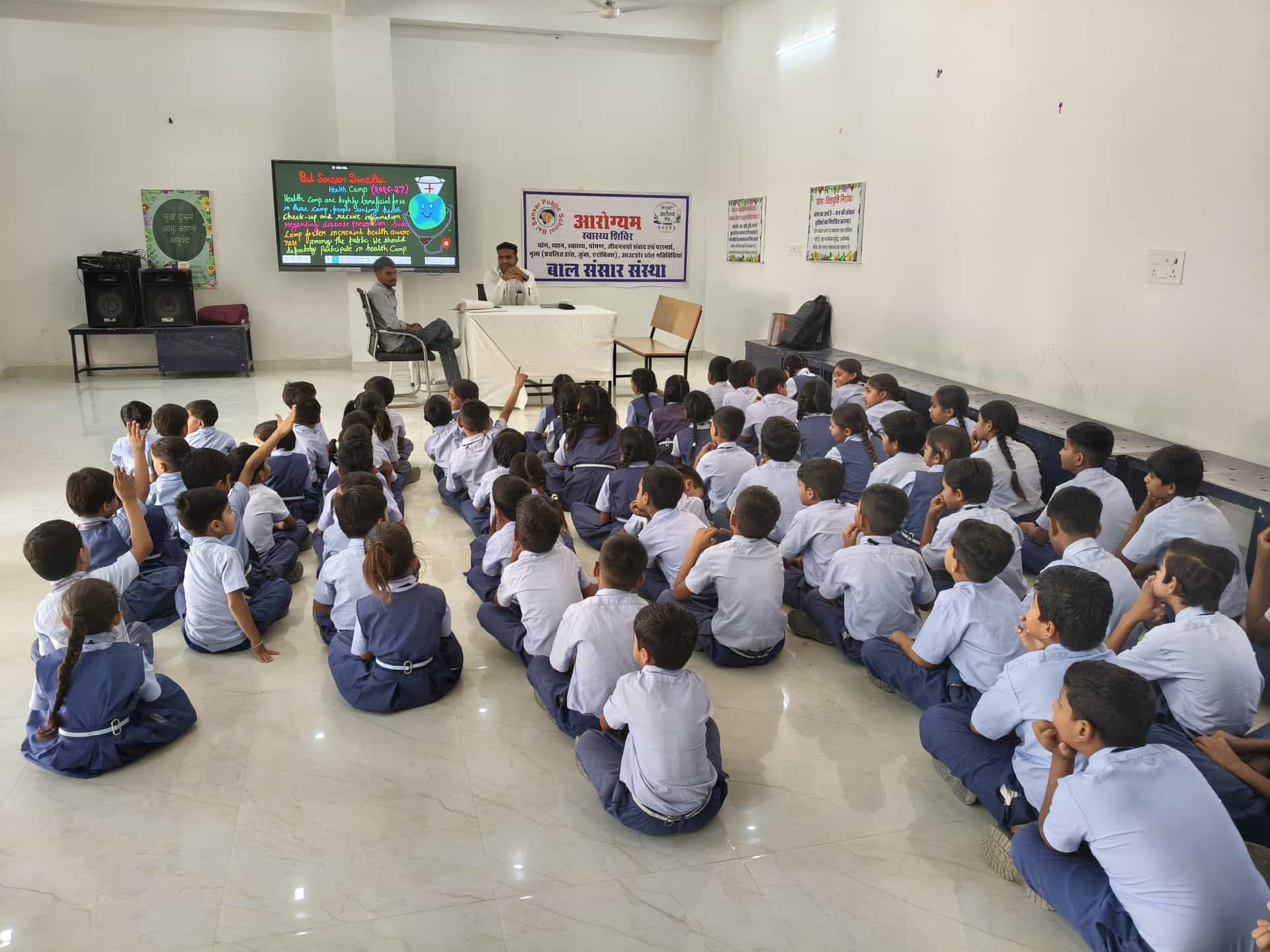 BSPS students seated in the school hall for an Aarogyam health camp session, several with hands raised