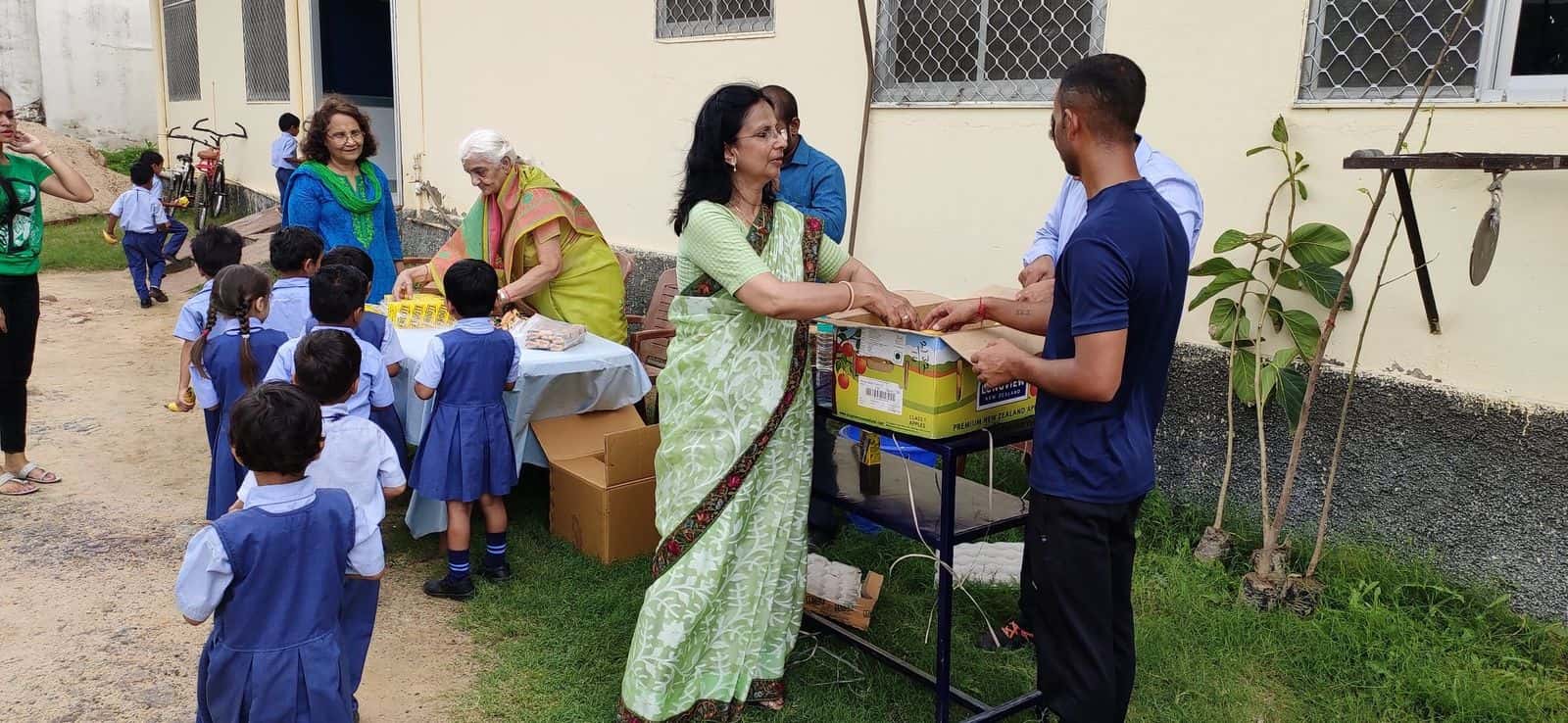 BSS staff and volunteers handing out bundles and fruit to BSPS children outside the school